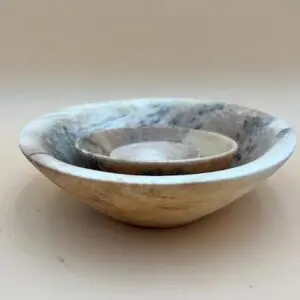 Two nested hand-crafted CHESTNUT NEST SET BOWLS on a beige surface, the smaller bowl sits inside the larger one, both featuring natural wood patterns.