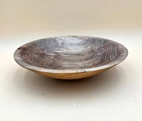 A simple Ambrosia Maple Artisan Bowl with natural grain patterns, placed on a light beige surface.